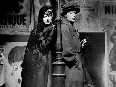 A woman and man leaning against a lamp post at night.