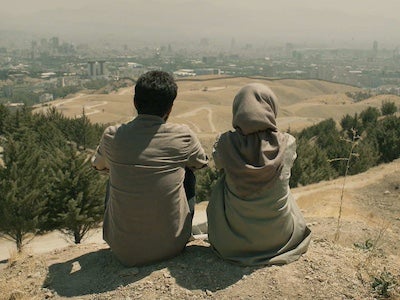 Two people sitting on soil and overlooking a landscape.
