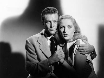 A man embracing a frightened woman, a shadow looming behind them.