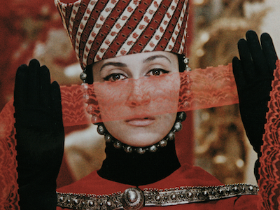 A person in elaborate costume holding a strip of lace in front of their face.