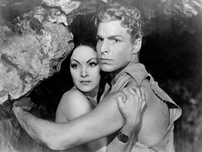 Actors Priscilla Lawson and Buster Crabbe with their arms wrapped around each other in a cave..