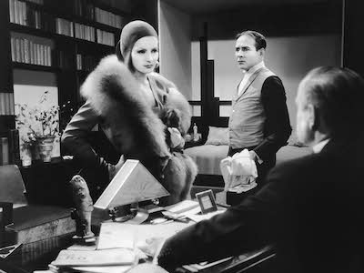 Greta Garbo facing a man seated at a desk in an office.