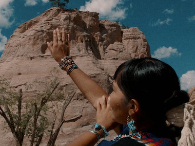 An Indigenous person raising an arm in a desert landscape.
