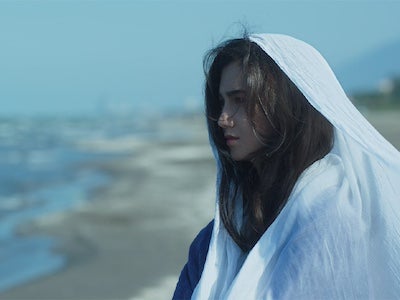 A woman draped in a cloth, looking towards the ocean.