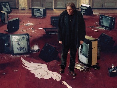 Actor Willem Dafoe standing among broken TVs.