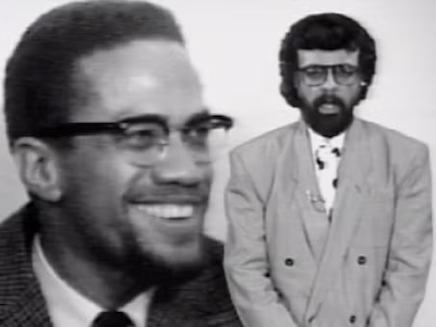 Tom Reed speaking to the TV audience with an image of Malcolm X in the background.