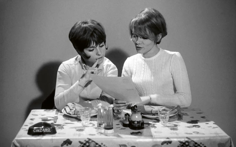 Two young women looking at a sheet of paper at a dining table.