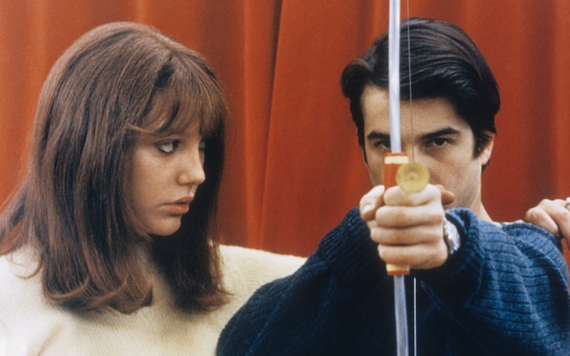 A woman looking at a man holding a bow and arrow.