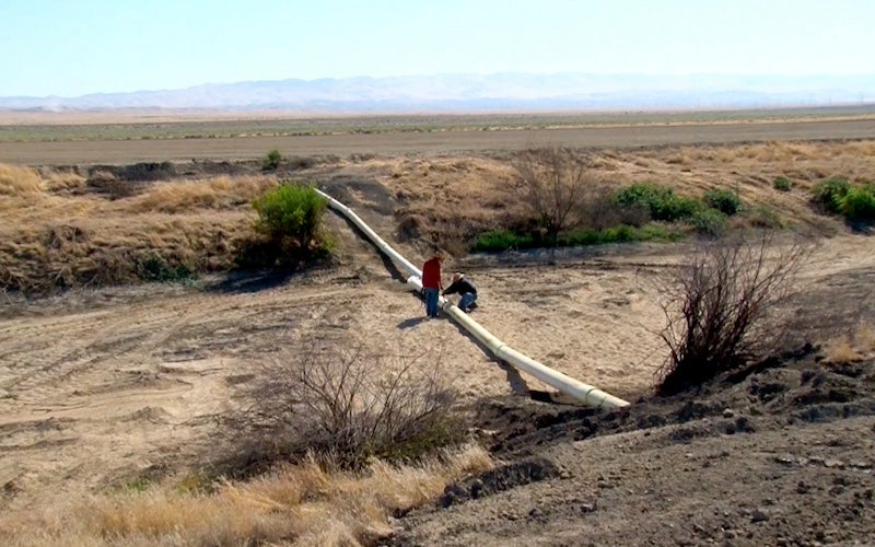 Two people examining a large pipe running through a desert.