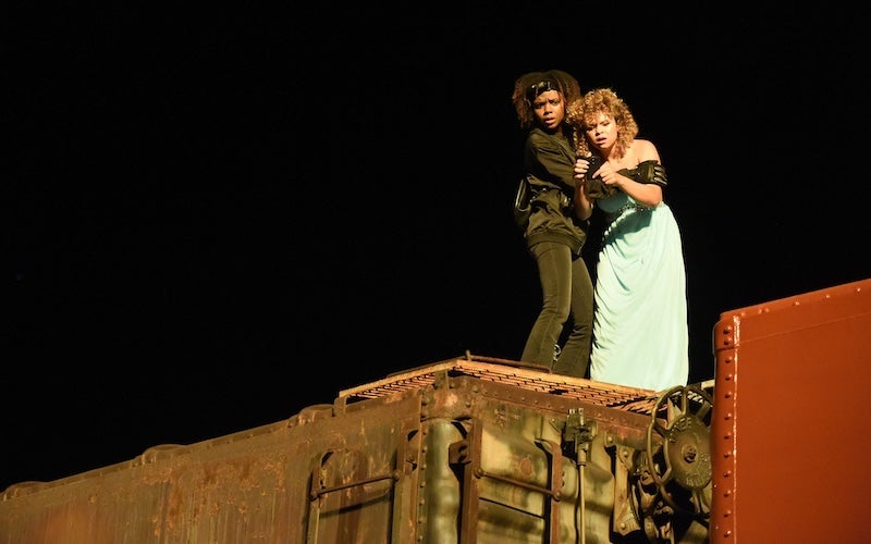 Two young women holding each other while standing on top of a train.