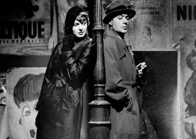 A woman and man leaning against a lamp post at night.