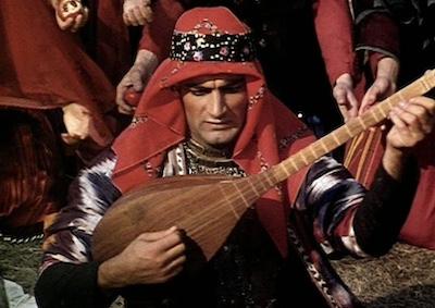 A man playing a stringed instrument and wearing a headdress.