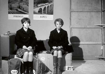 Two young women sitting on suitcases.