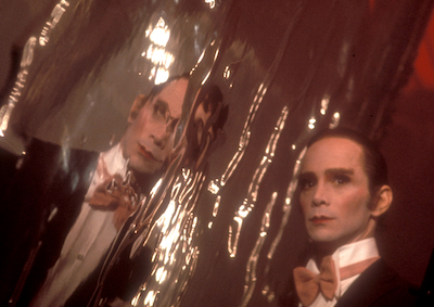 Joel Grey leaning towards a reflective wall in Cabaret.