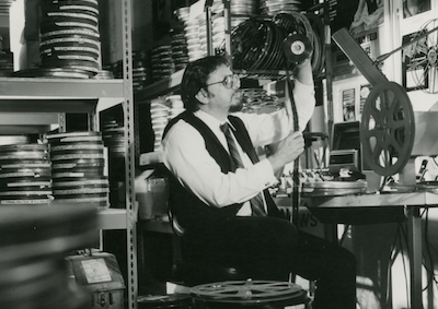 Robert Rosen looking at a piece of film, surrounded by film cans.