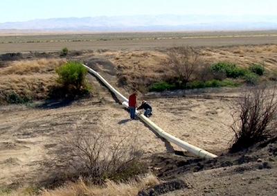 Two people looking at a large pipe in a desert landscape.