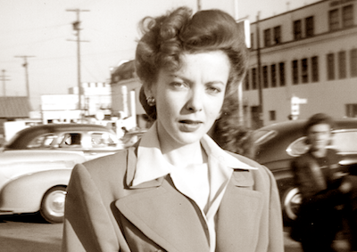 Candid photo of Ida Lupino standing by a parking lot.