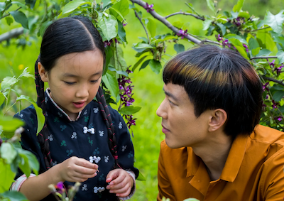 A man kneeling next to a young girl under a tree.