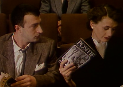 A man and woman sitting in a movie theater, holding film magazines.