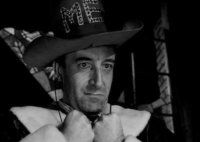 Actor Peter Sellers with a grim expression, wearing a hat decorated with the word "ME."