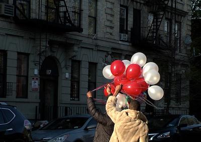 Two people holding red and white balloons in the street.