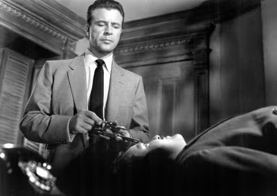 Dick Powell looking down at an unconscious man.