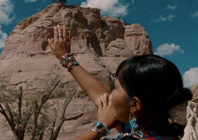 An Indigenous person raising an arm in a desert landscape.