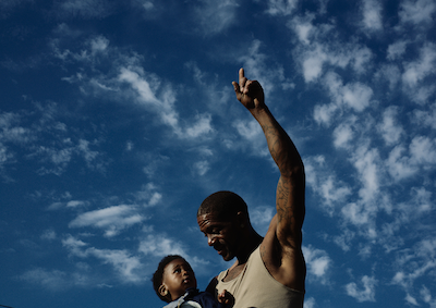 A man pointing at the sky and holding a baby.