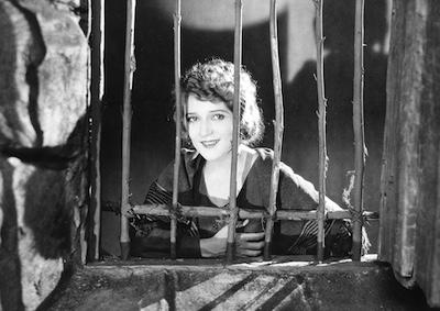 Mary Pickford smiling behind a window.