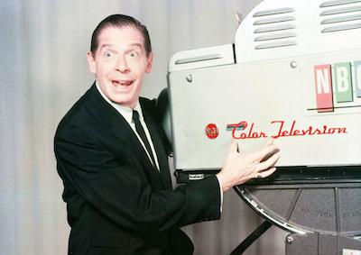 Milton Berle posing with an NCB Color Television camera.