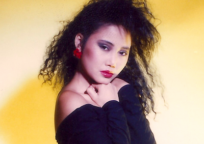 A young woman posing in 1980s hair and fashion.