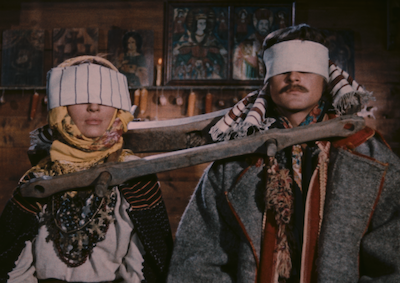 A man and woman blindfolded and tethered together by a yoke.