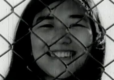 A young woman smiling behind a chainlink fence.