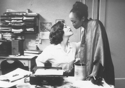 Two women leaning in to kiss in an office.