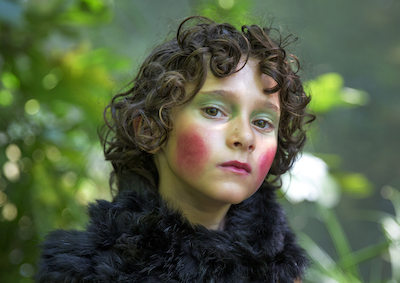 A young girl wearing exaggerated makeup and a furry scarf.