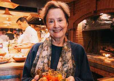 Alice Waters smiling and holding persimmons.