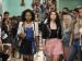Two teenage girls walking down a school hall as other teens stare.