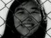 A young woman smiling behind a chainlink fence.